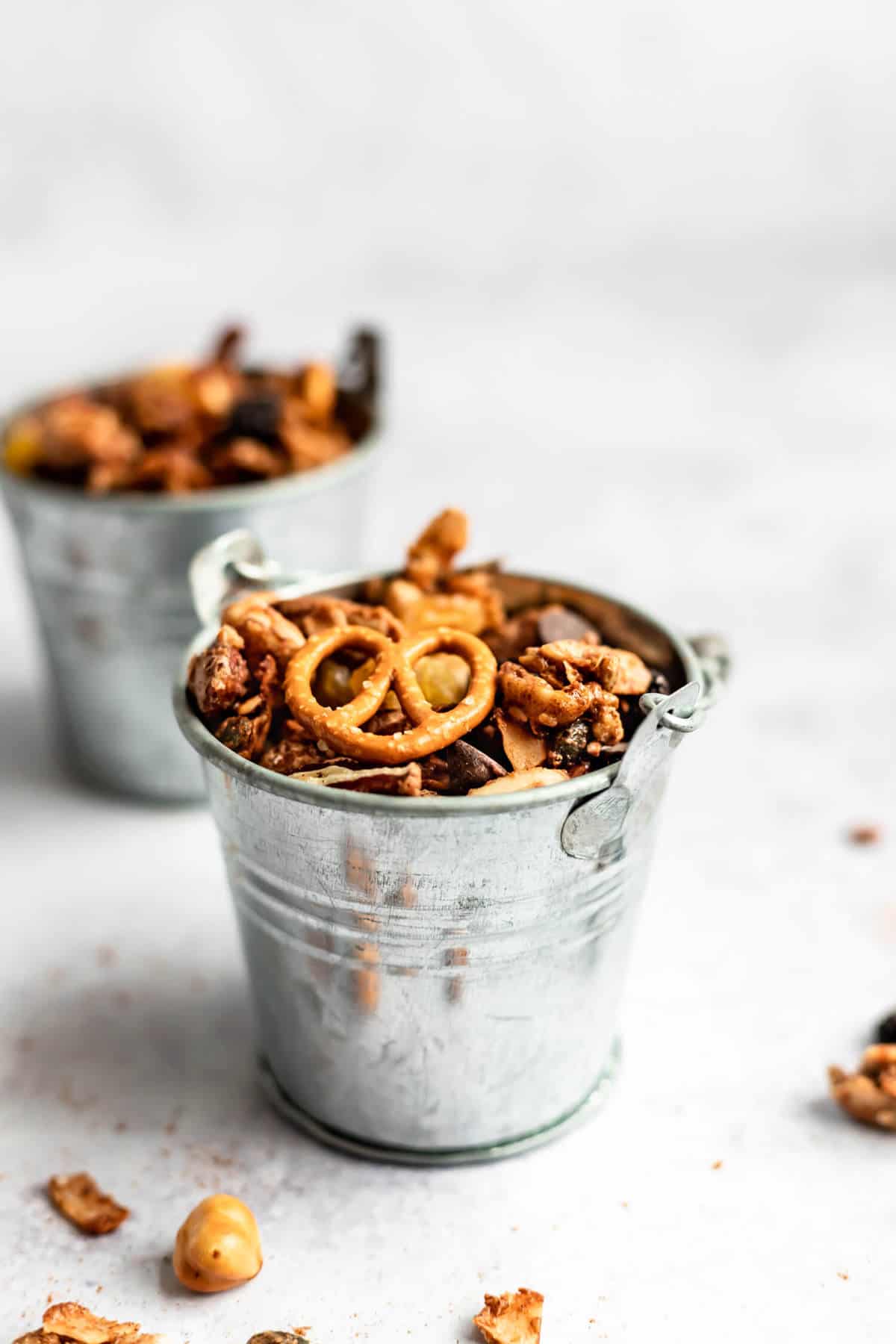 a small metal bucket filled with nutty snack mix and pretzels with a few pieces scattered around