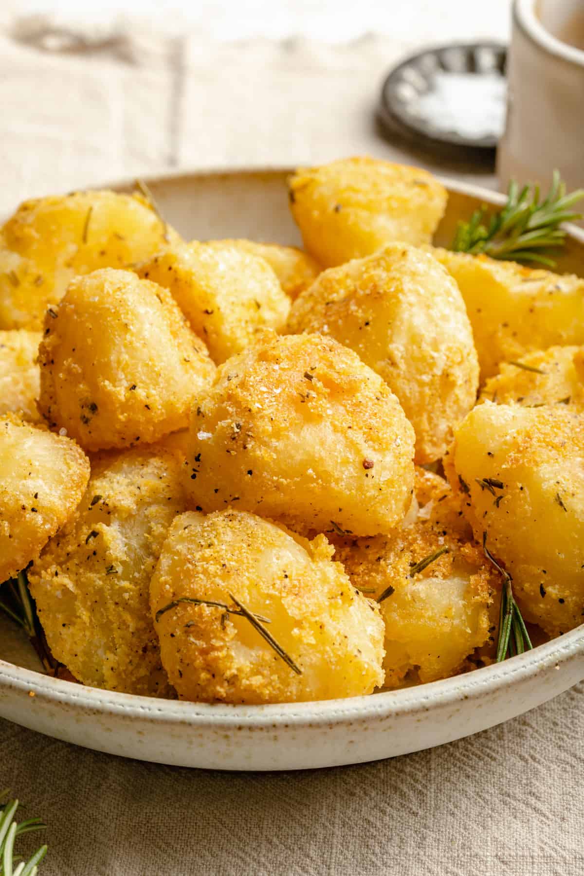 A bowl of super crispy roasted potatoes with sprigs of rosemary around. 